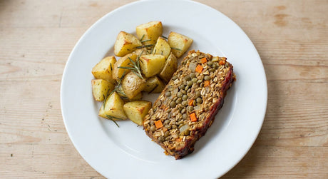 Slice of vegan lentil loaf with roasted rosemary potatoes on a white plate
